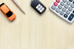 A toy car, a pen, a car key fob, and a calculator laid out on a wood desk to represent buying a car near Orangeburg, South Carolina