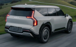 A silver 2024 Kia EV9 driving down a narrow road surrounded by grassy hills near Orangeburg, South Carolina