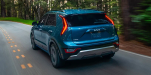 A blue 2025 Kia Niro Plug-in Hybrid driving down a wooded road near Orangeburg, South Carolina